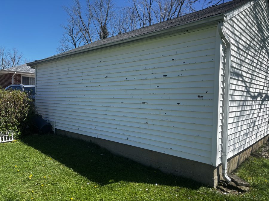 Hail-damaged vinyl siding with impact punctures across the panels